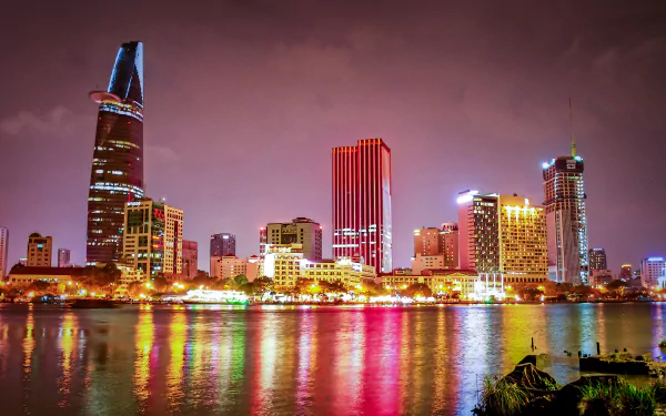 Night view of Ho Chi Minh City skyline along the Saigon River, featuring illuminated skyscrapers including the Bitexco Financial Tower in Vietnam.