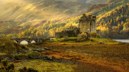 Sunbeam illuminates Eilean Donan Castle surrounded by vibrant fall foliage in a scenic Scottish landscape.