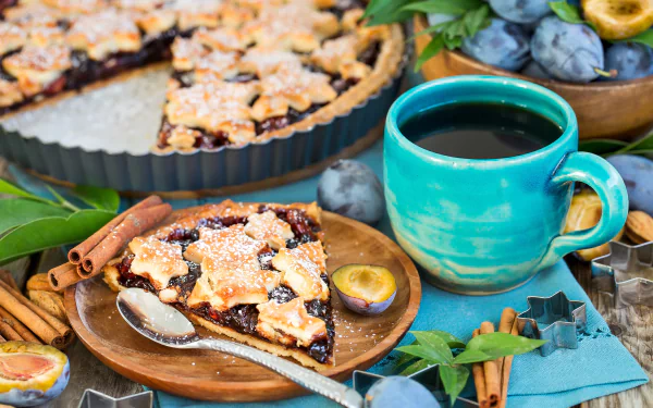 A 4K Ultra HD still life featuring a slice of plum pie dusted with powdered sugar, a blue cup of coffee, fresh plums, cinnamon sticks, and a pastry in the background.