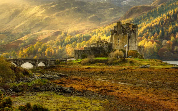 Sunbeam illuminates Eilean Donan Castle surrounded by vibrant fall foliage in a scenic Scottish landscape.