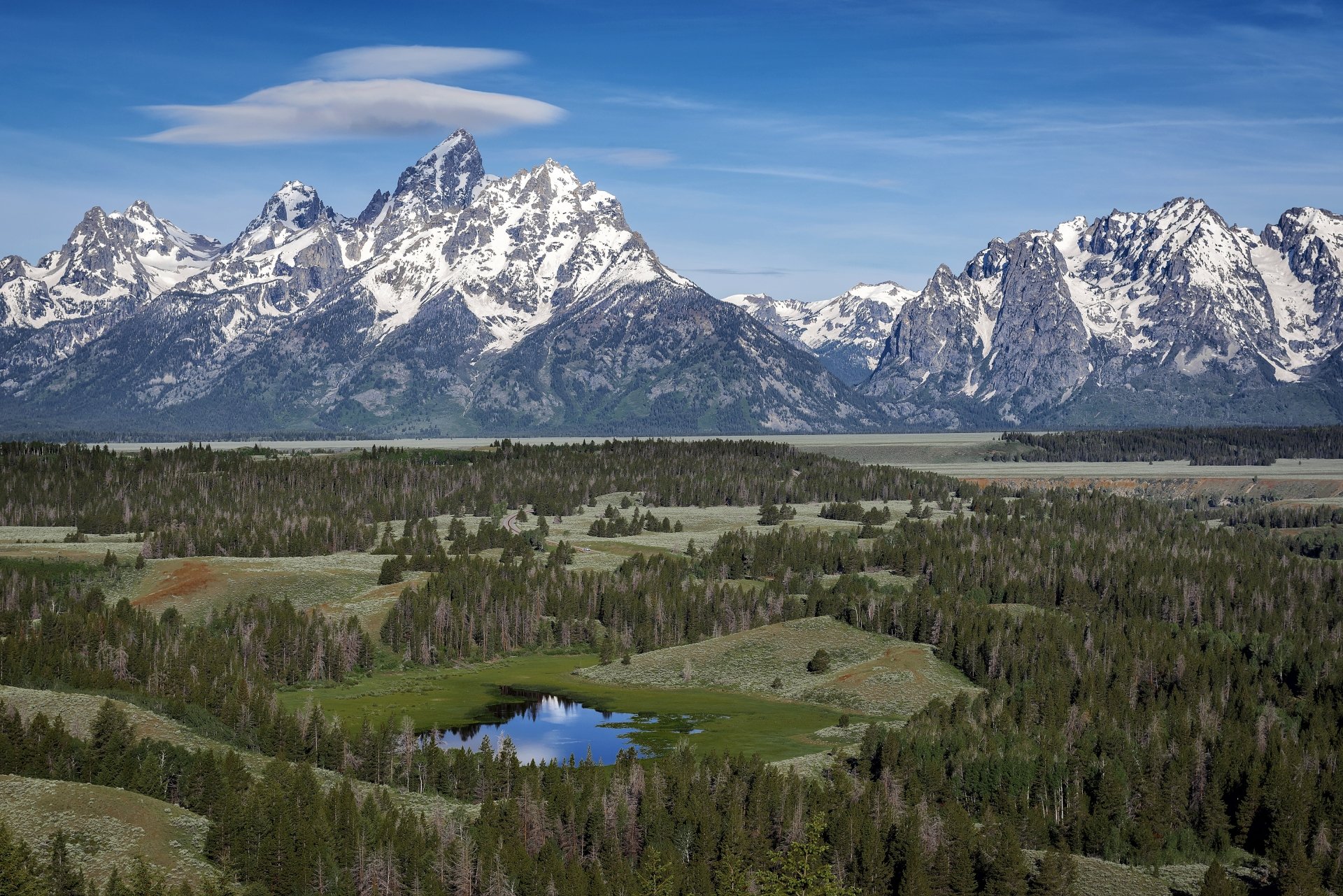 4K Ultra HD PC desktop wallpaper/background: panoramic mountain and nature landscape with snow-capped peaks, dense forest, meadow and a reflective alpine pond under a clear blue sky.