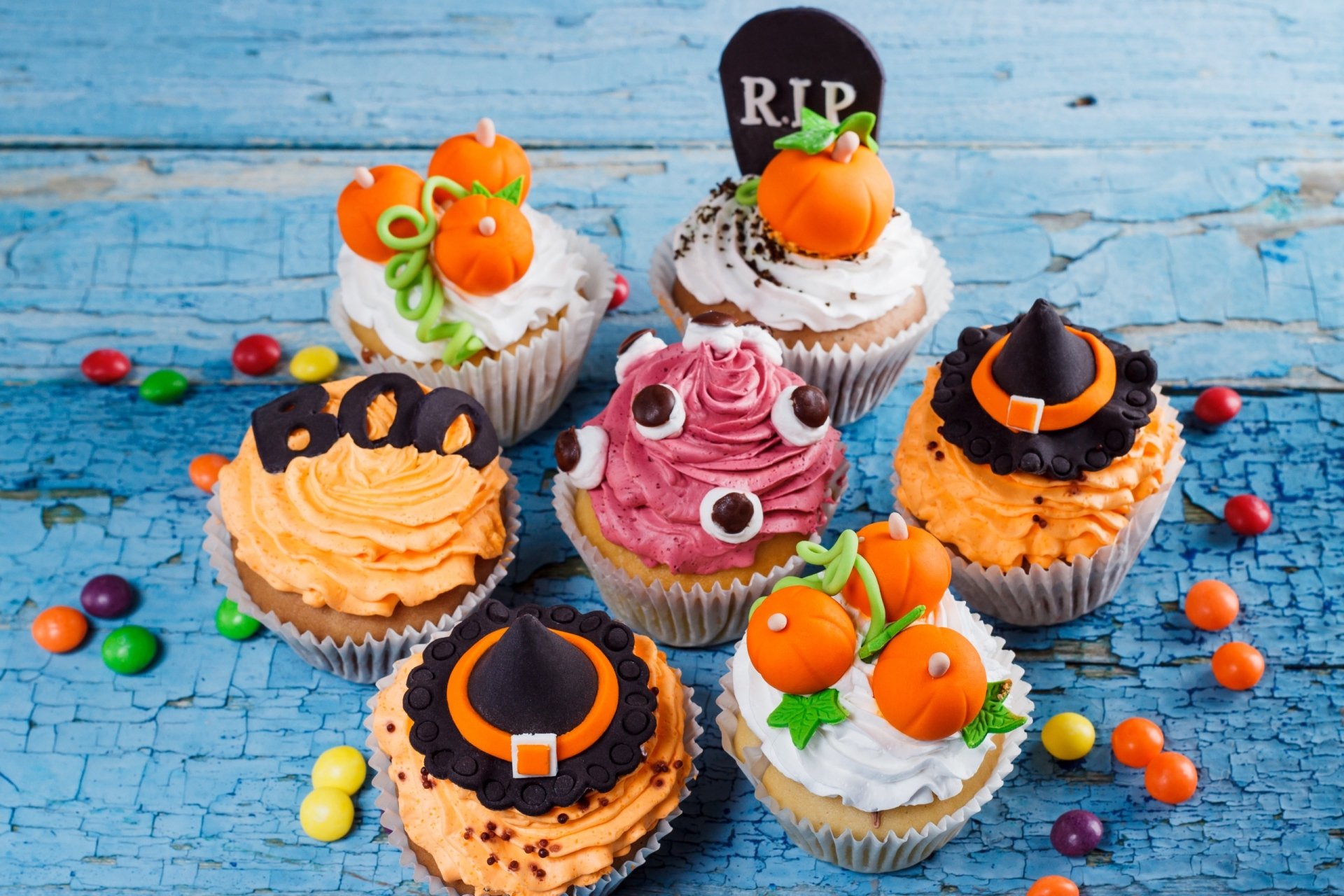 HD Halloween holiday desktop wallpaper featuring festive cupcakes decorated with pumpkins, witch hats, googly eyes, and a tombstone on a rustic blue wooden surface.