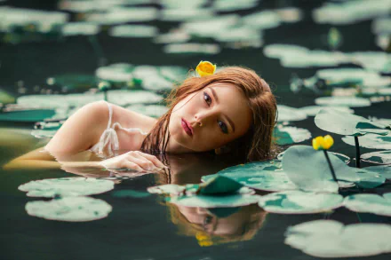 A woman with lipstick lies in a pond surrounded by lily pads, reflecting on the water's surface. A flower adorns her hair, creating a serene, natural HD desktop wallpaper background.
