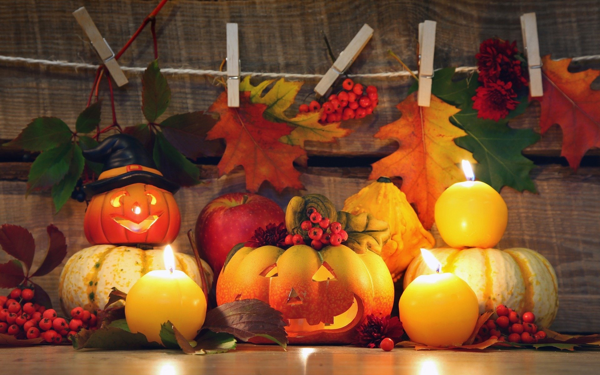 HD PC desktop wallpaper featuring a Halloween holiday scene with carved pumpkins, candles, autumn leaves, and berries against a wooden background.
