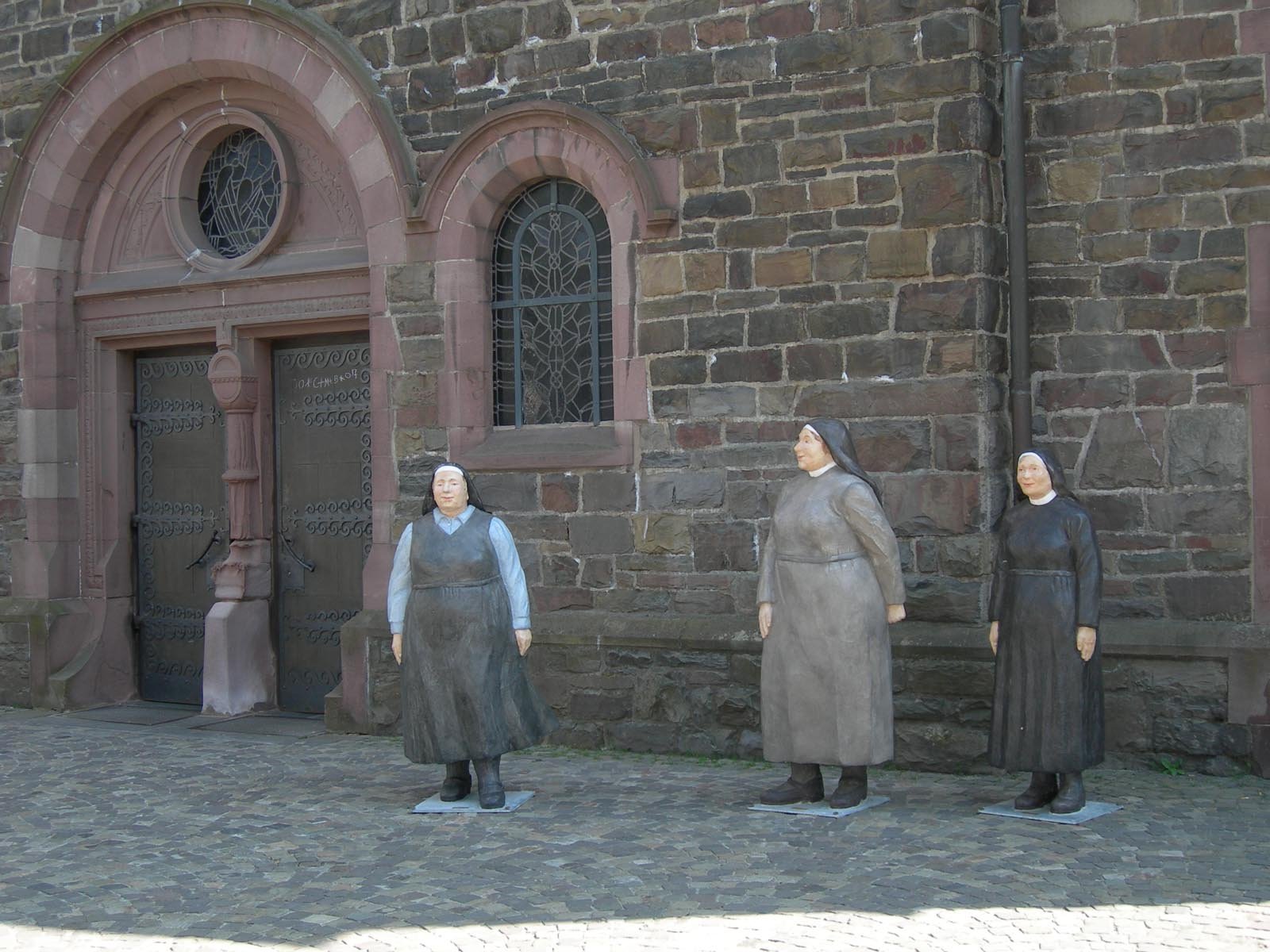 HD wallpaper of a religious Christian statue outside a church, featuring three female figures in front of a stone facade with arched doors and windows.