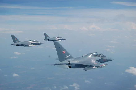 Three Yakovlev Yak-130 military jet fighter warplanes flying in formation above the clouds against a blue sky, captured in high-definition desktop wallpaper quality.