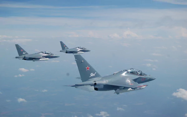 Three Yakovlev Yak-130 military jet fighter warplanes flying in formation above the clouds against a blue sky, captured in high-definition desktop wallpaper quality.