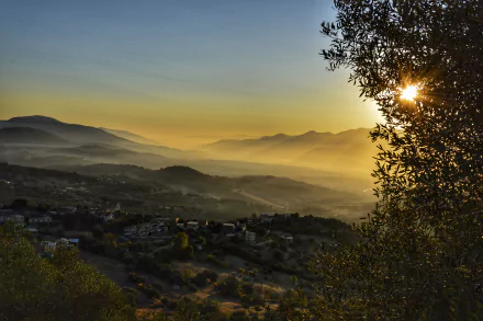 5K Ultra HD PC desktop wallpaper: sunrise over Bejaia mountains, misty valleys and a man-made village below, sun peeking through trees at right.