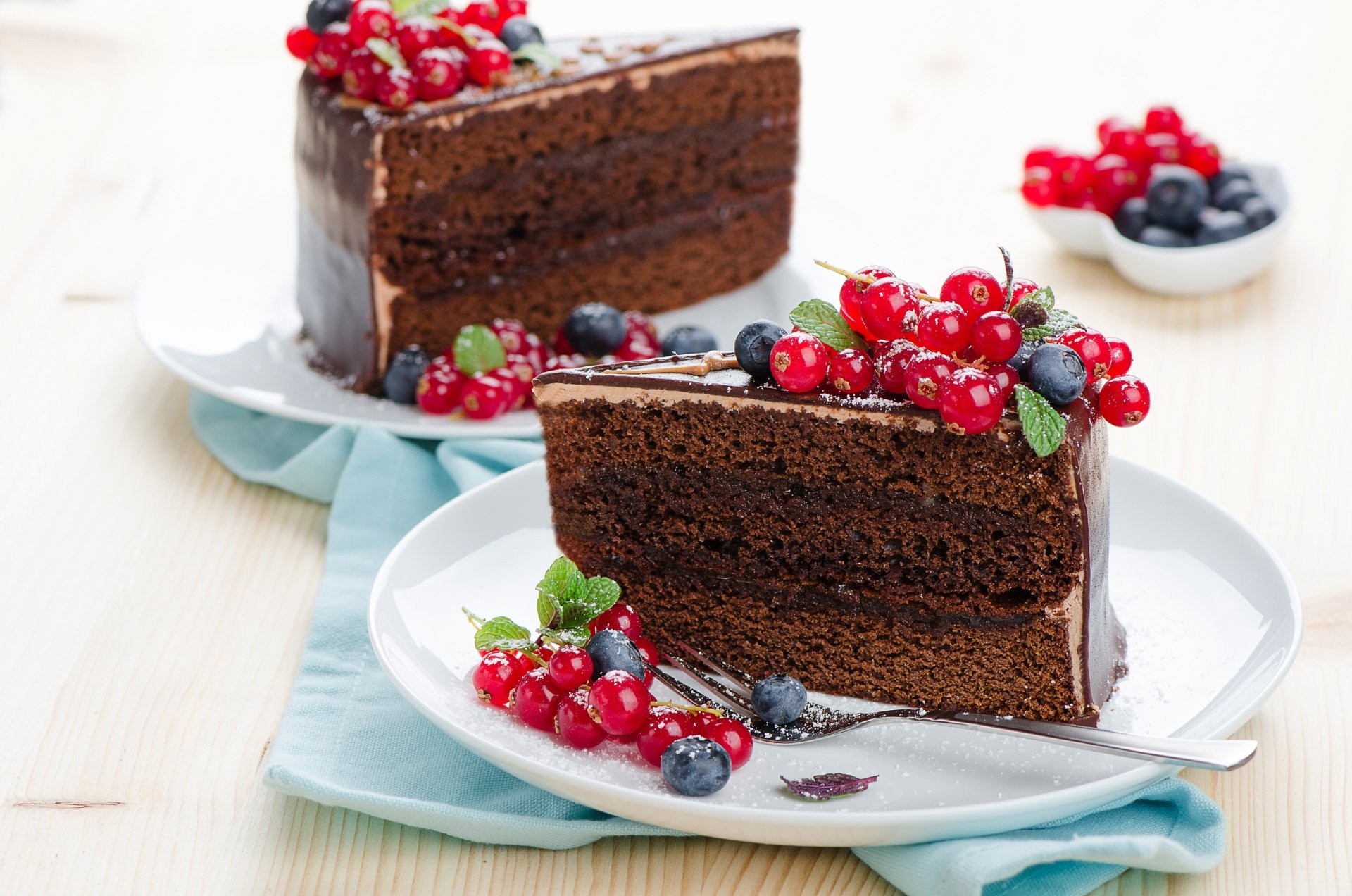 A rich chocolate cake slice garnished with fresh blueberries, red currants, and mint leaves, styled as a vibrant 4K Ultra HD desktop wallpaper dessert background.
