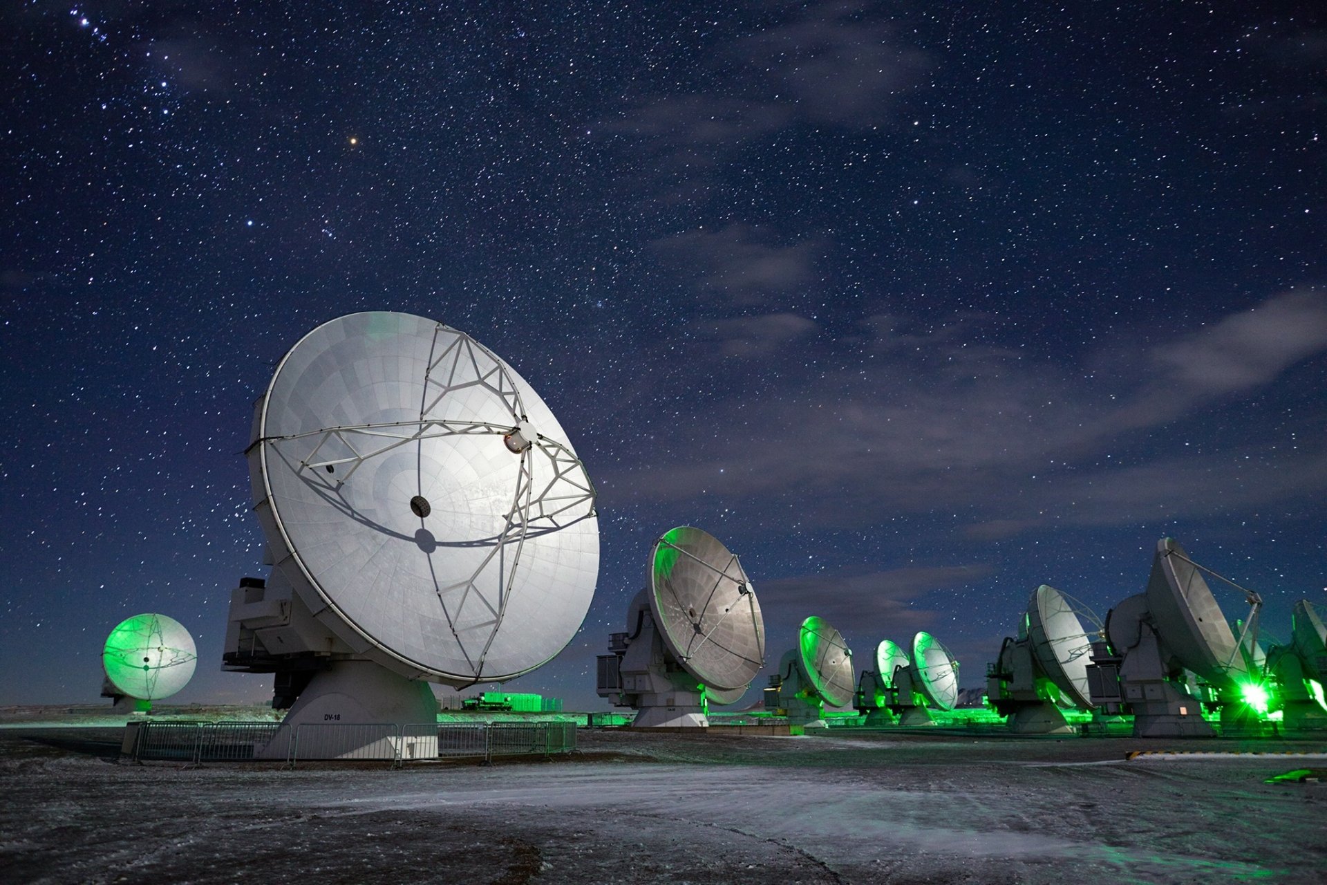 Night sky filled with stars above a row of large military satellite dishes and telescopes, captured in high-definition for a PC desktop wallpaper.