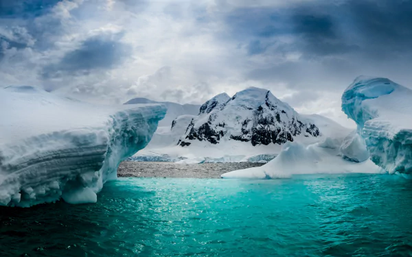 Snow-covered mountains and glaciers rise above icy turquoise waters on Half Moon Island, Antarctica, showcasing pristine nature in this HD desktop wallpaper.