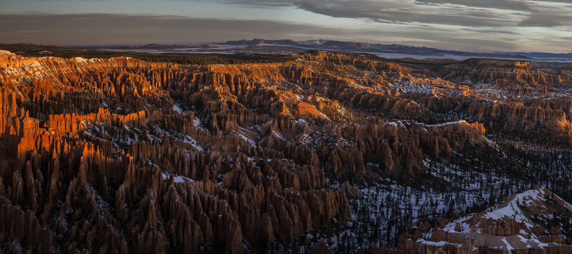 A stunning 4K Ultra HD winter landscape of Bryce Canyon National Park in the USA, showcasing snow-dusted canyon formations and rugged mountain terrain under a moody sky.