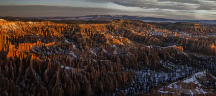 A stunning 4K Ultra HD winter landscape of Bryce Canyon National Park in the USA, showcasing snow-dusted canyon formations and rugged mountain terrain under a moody sky.
