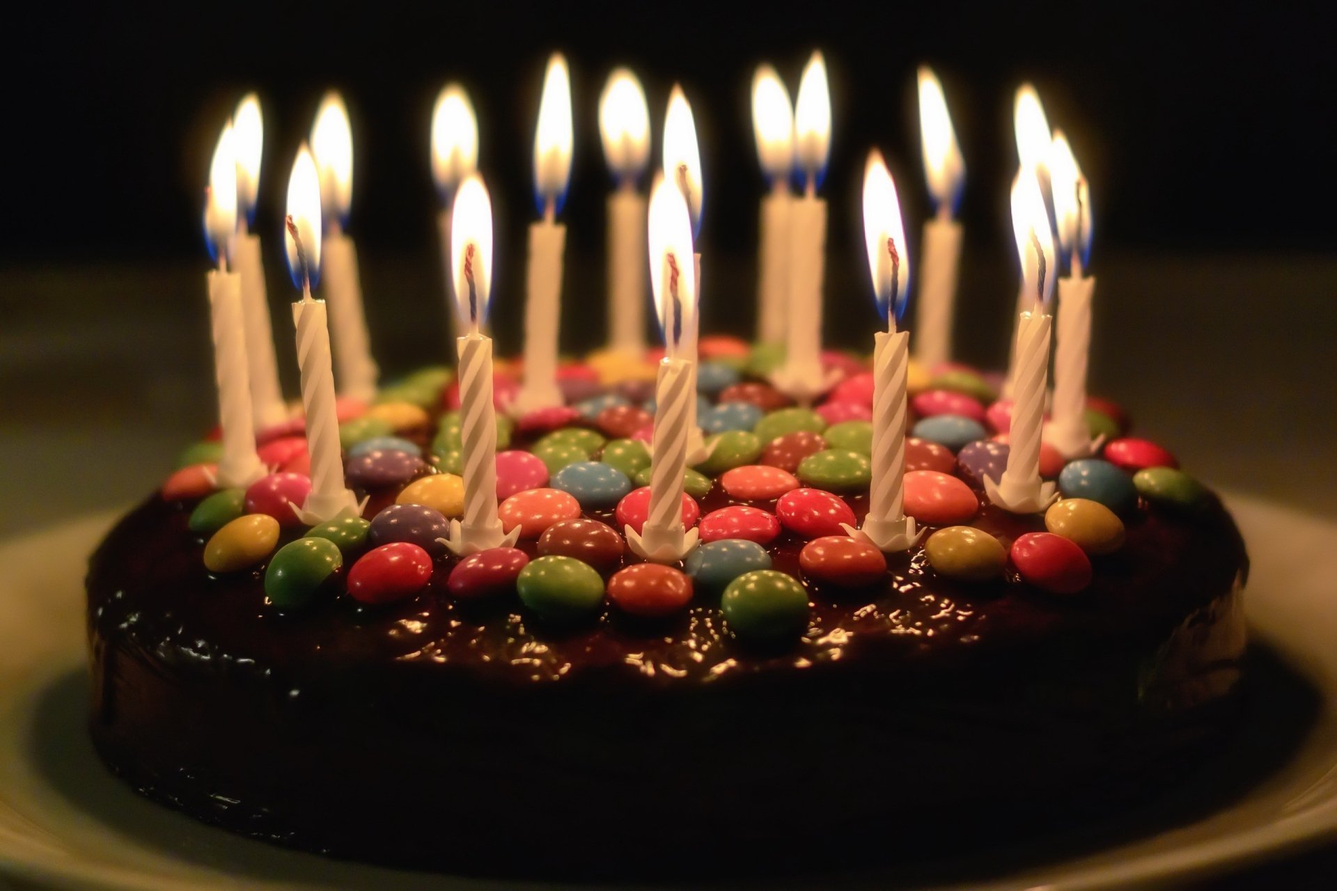 HD desktop wallpaper of a birthday cake decorated with colorful candy and topped with lit candles, capturing a festive holiday celebration atmosphere.