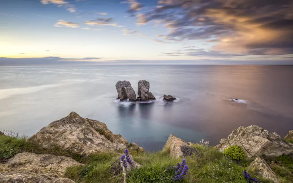 A natural rock arch rises from the ocean under a vibrant sky at the horizon, captured in a high-definition desktop wallpaper showcasing stunning nature scenery.
