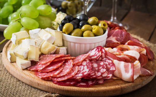 A 4K Ultra HD still life of a wooden platter with olives, green grapes, sliced cheese, and assorted cured meats, set as a PC desktop wallpaper and background.