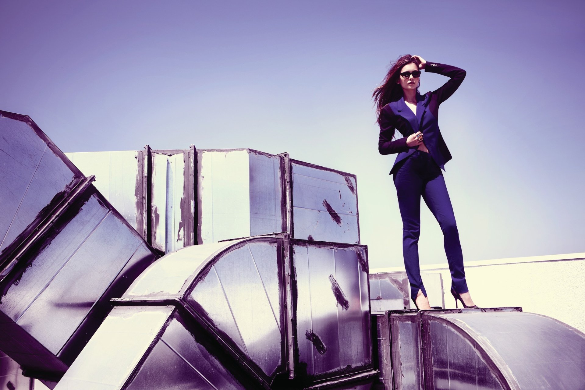 HD desktop wallpaper featuring Canadian actress Nina Dobrev, a brunette wearing sunglasses, standing confidently on reflective industrial structures.