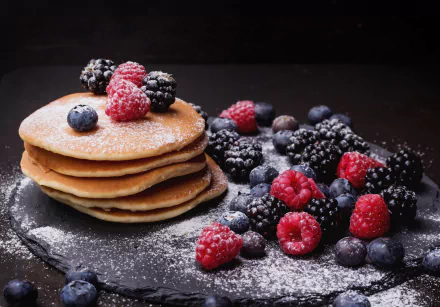 HD desktop wallpaper featuring a stack of pancakes dusted with powdered sugar, accompanied by fresh blueberries, blackberries, and raspberries, creating a vibrant breakfast scene.