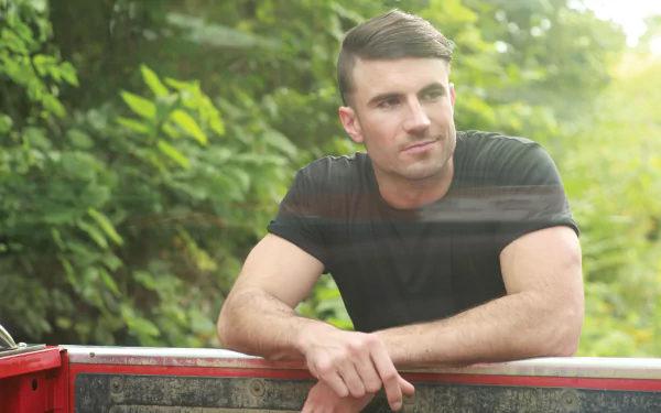 HD wallpaper of a contemplative man leaning on a red truck, surrounded by greenery.