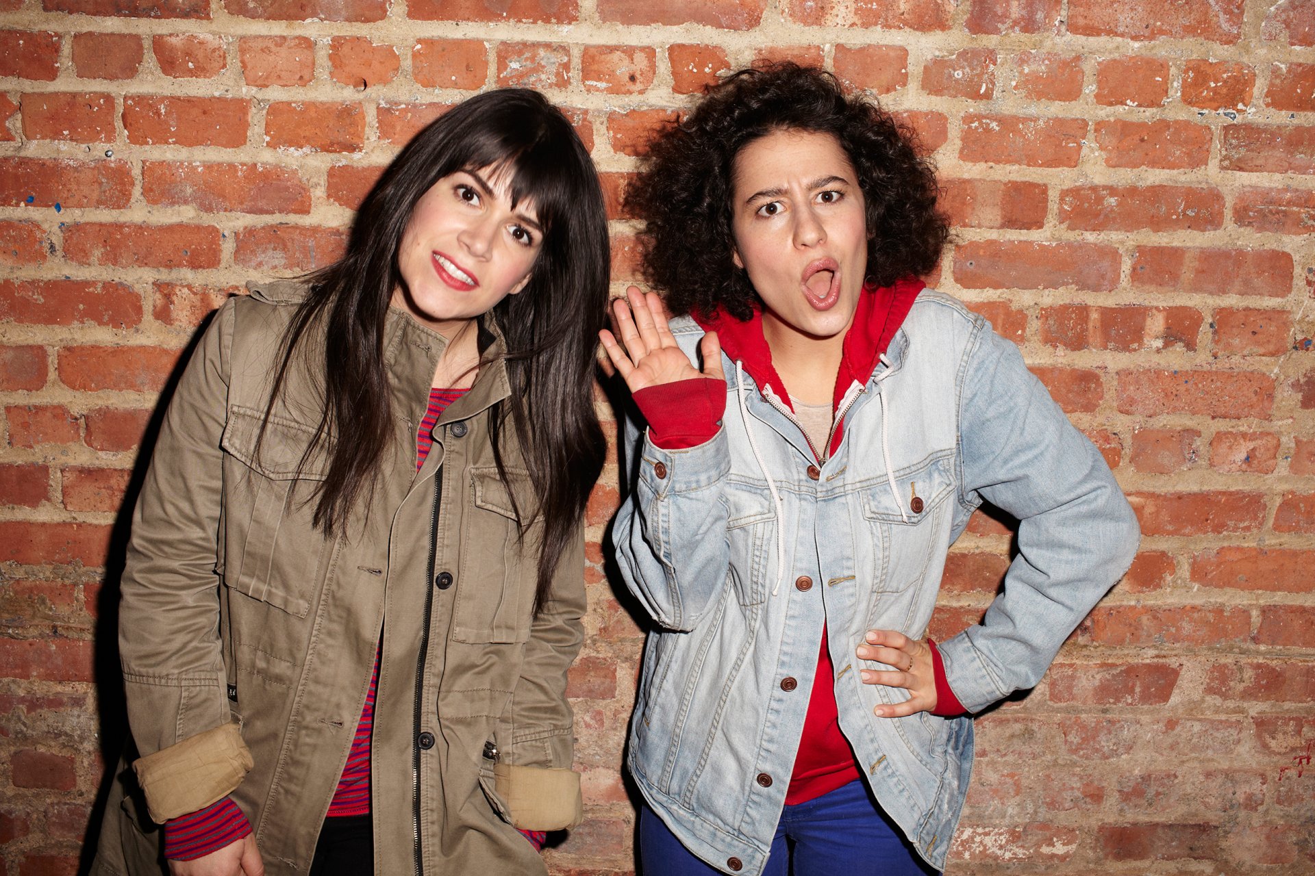 HD desktop wallpaper featuring two women from Broad City in front of a brick wall, one waving and the other making a surprised face.