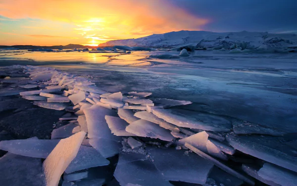 Sunset over an icy glacier in Iceland, showcasing winter's frozen beauty with cracked ice sheets reflecting warm golden light in this HD desktop wallpaper.