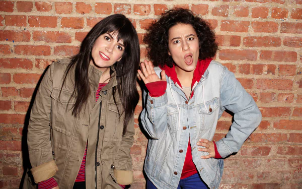 HD desktop wallpaper featuring two women from Broad City in front of a brick wall, one waving and the other making a surprised face.
