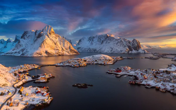 Winter view of Reine town surrounded by snow-covered mountains and a calm lake in Norway’s Lofoten, captured in vibrant colors for an HD desktop wallpaper.