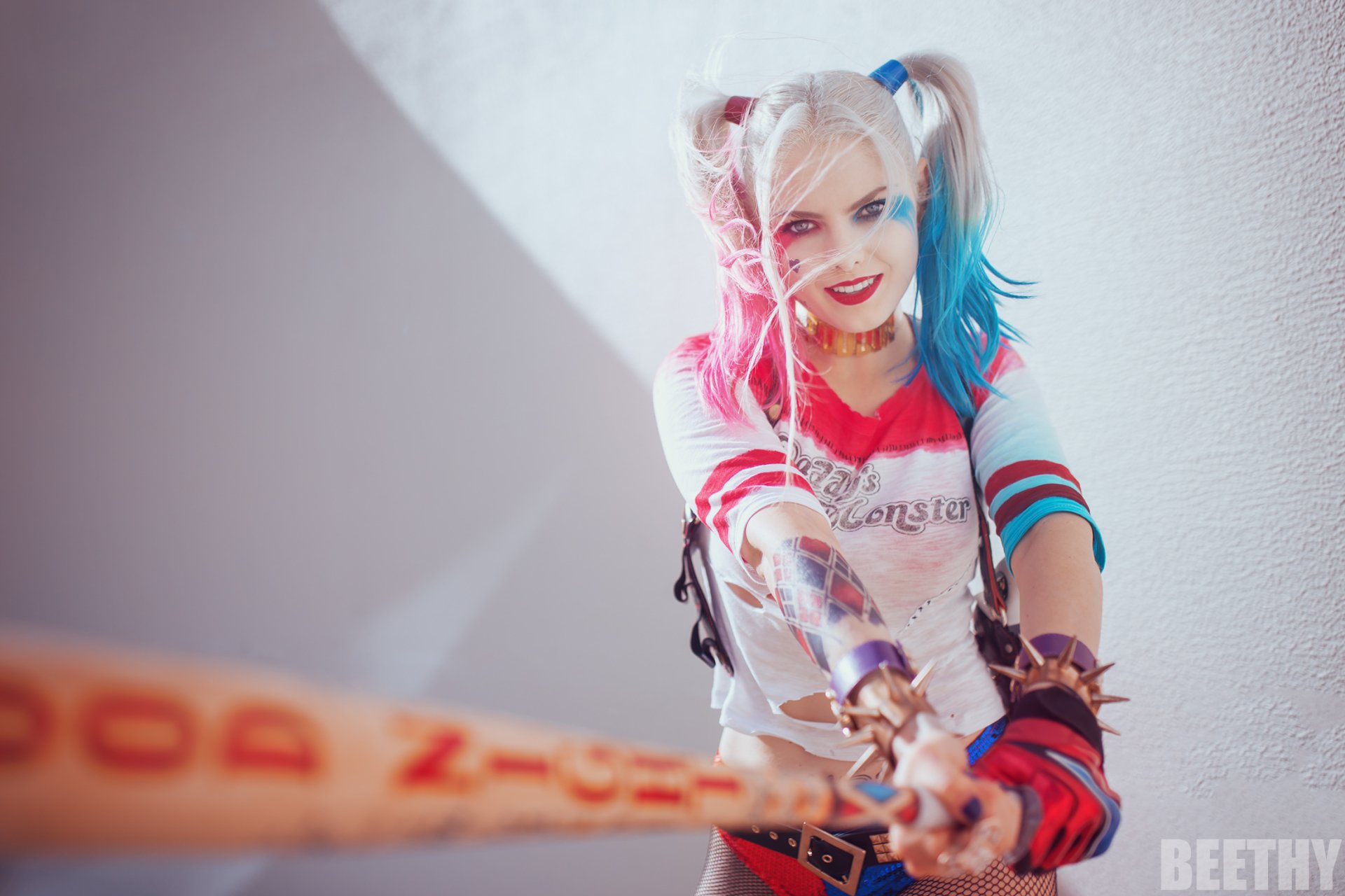 HD PC desktop wallpaper featuring a woman cosplaying as Harley Quinn, holding a baseball bat and smiling against a plain light background.