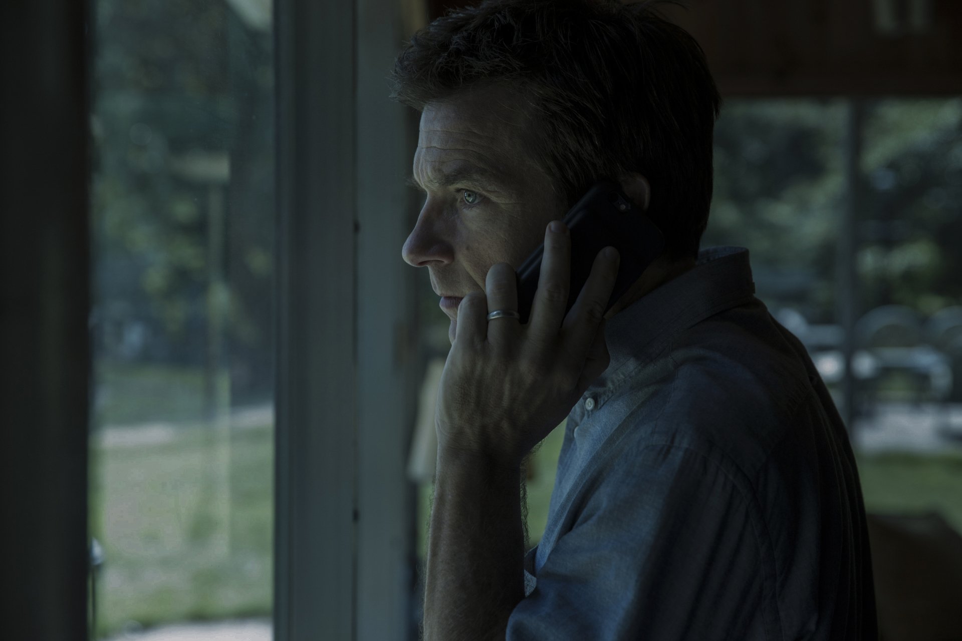 HD wallpaper featuring Jason Bateman from Ozark talking on the phone near a window, in a moody, cinematic setting.