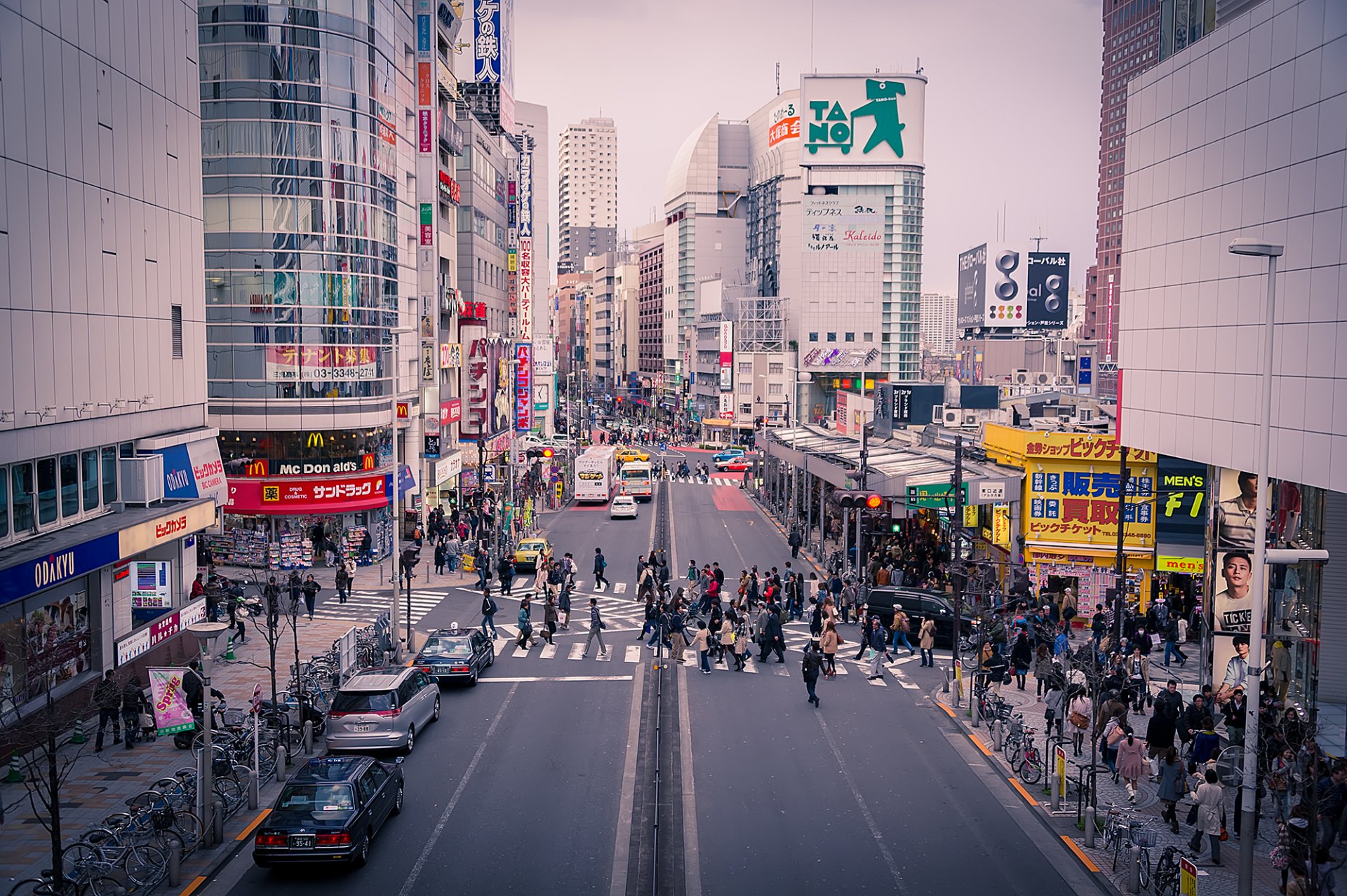 HD desktop wallpaper of bustling Shinjuku district in Tokyo with crowded sidewalks and traffic on the streets.
