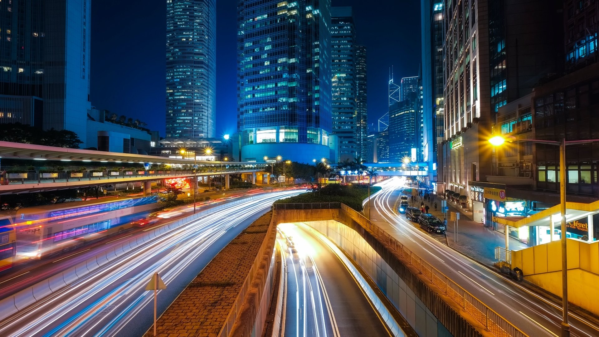 Nighttime cityscape of Hong Kong showcasing illuminated skyscrapers and vibrant light trails from traffic in a time-lapse style HD wallpaper.