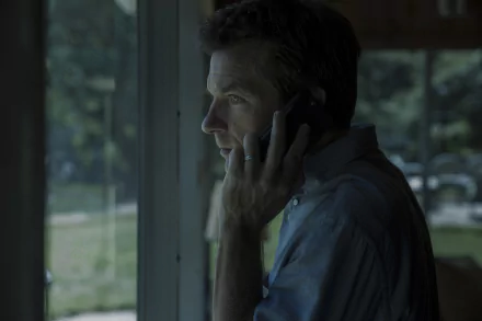 HD wallpaper featuring Jason Bateman from Ozark talking on the phone near a window, in a moody, cinematic setting.