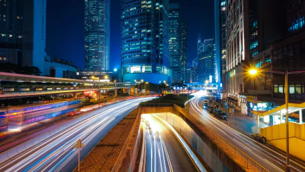 Nighttime cityscape of Hong Kong showcasing illuminated skyscrapers and vibrant light trails from traffic in a time-lapse style HD wallpaper.