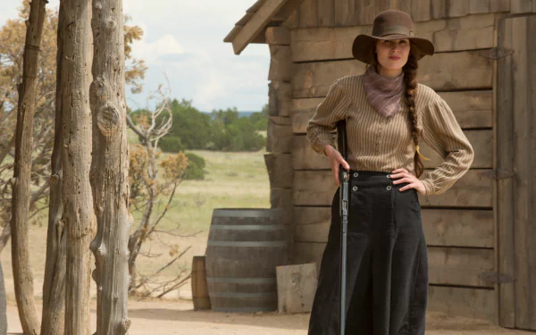 HD desktop wallpaper from Godless featuring a confident woman in vintage Western attire standing beside a wooden cabin.