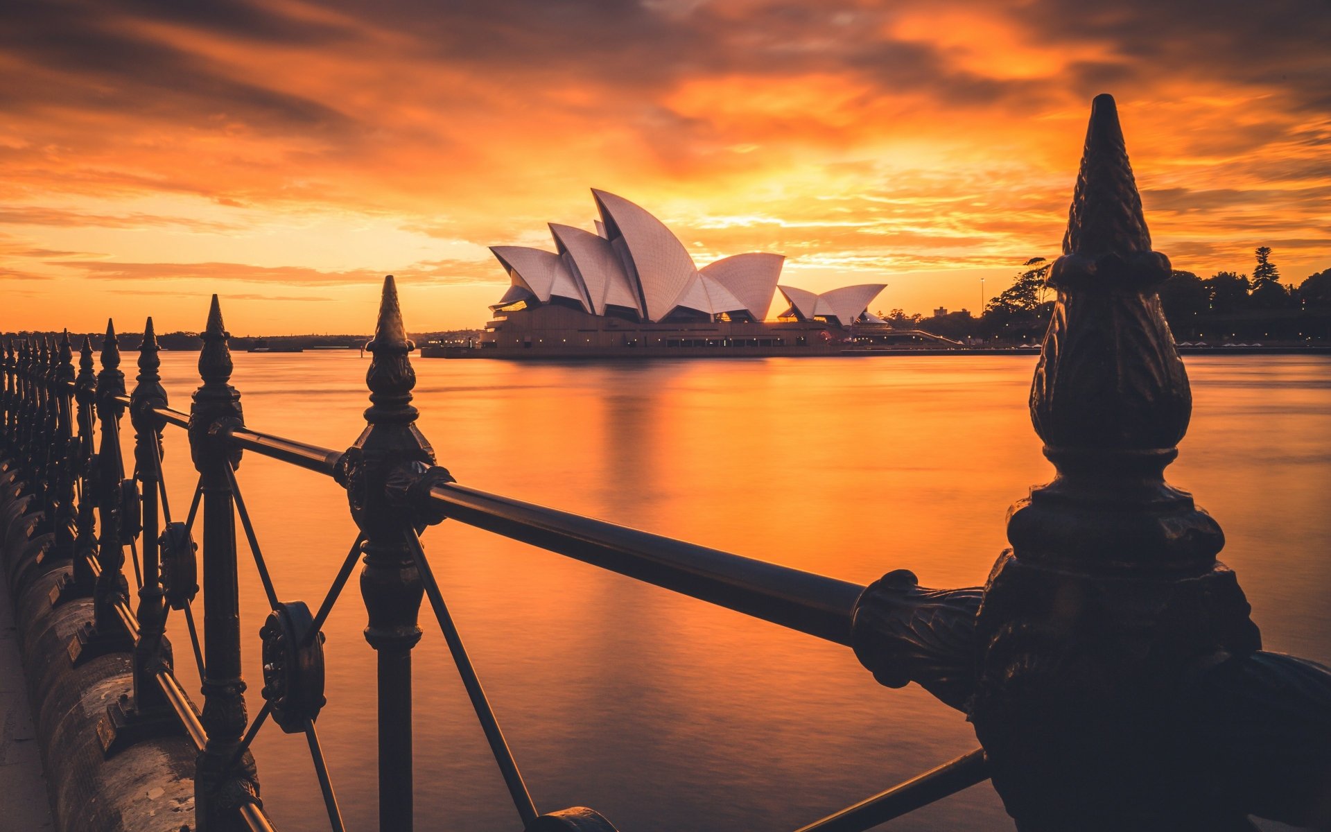 Sunset view of the man-made Sydney Opera House in Australia, framed by silhouetted railing, captured in stunning 4K Ultra HD for a PC desktop wallpaper.