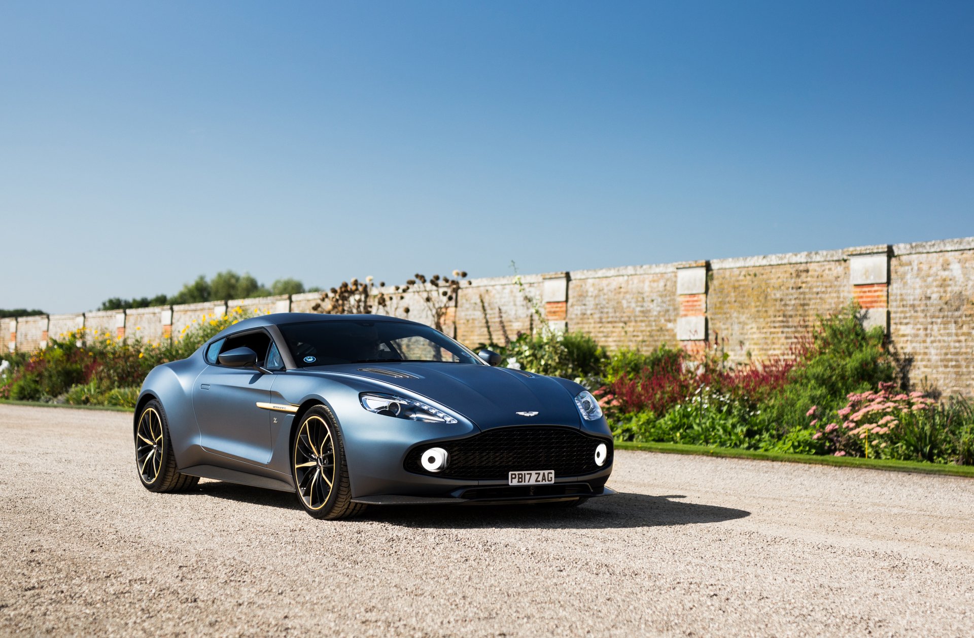 Aston Martin Vanquish supercar grand tourer on a sunlit road by a brick wall — 4K Ultra HD PC desktop wallpaper