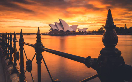 Sunset view of the man-made Sydney Opera House in Australia, framed by silhouetted railing, captured in stunning 4K Ultra HD for a PC desktop wallpaper.