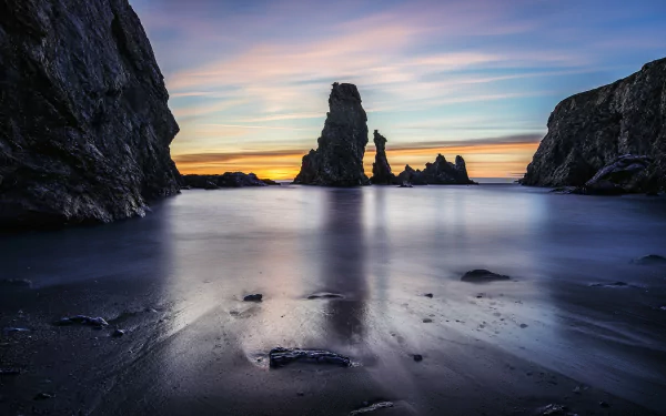 2K Quad HD PC desktop wallpaper: French beach at sunset with jagged sea stacks framed by cliffs, smooth reflective wet sand and pastel sky — nature scene in France.