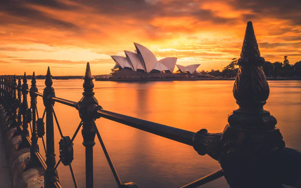 Sunset view of the man-made Sydney Opera House in Australia, framed by silhouetted railing, captured in stunning 4K Ultra HD for a PC desktop wallpaper.