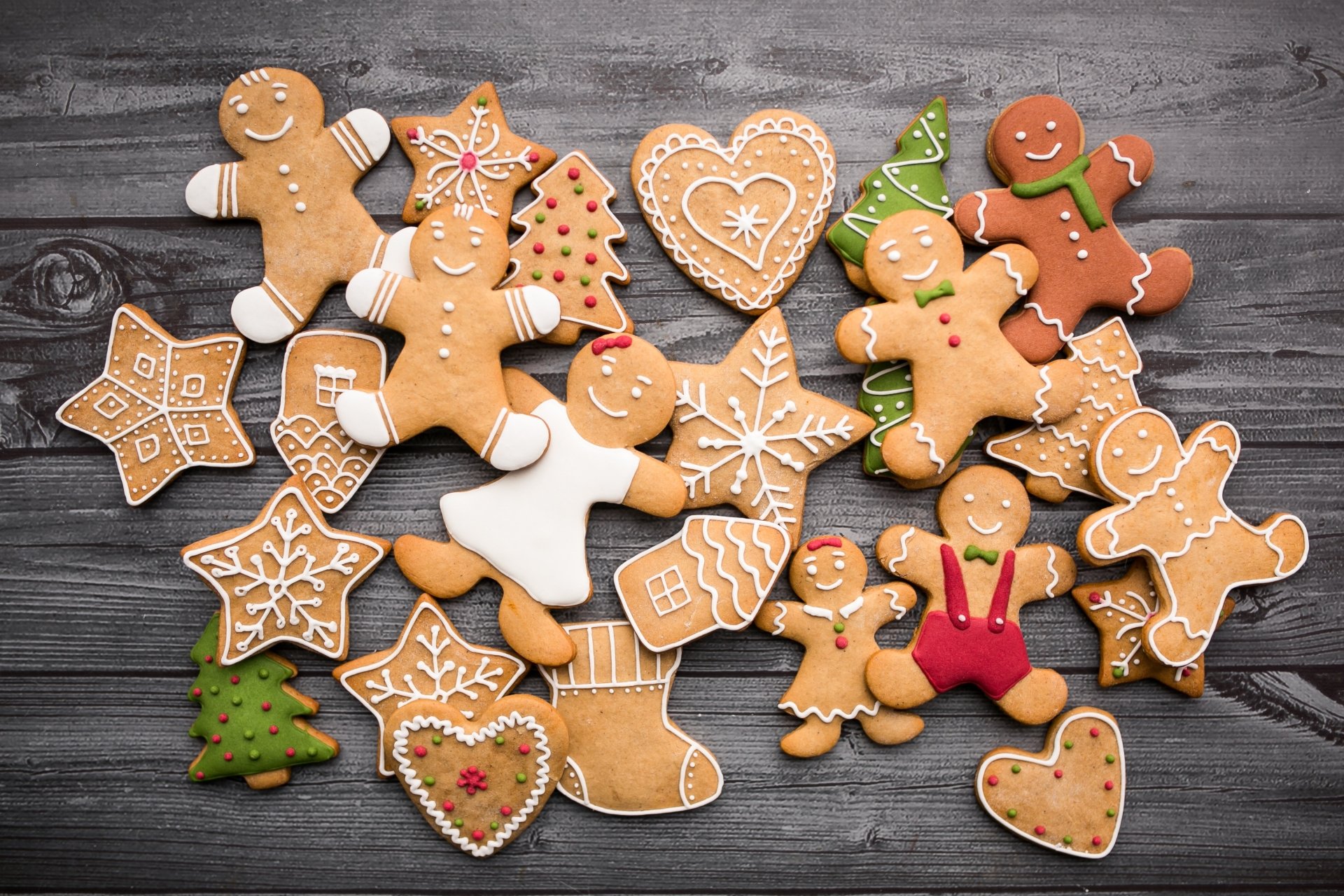 HD PC desktop wallpaper featuring an assortment of decorated gingerbread cookies shaped like people, stars, hearts, and Christmas trees on a rustic wooden background.