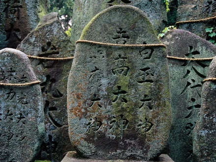 HD desktop wallpaper showing weathered, moss-covered stone statues engraved with Japanese characters, highlighting intricate man-made craftsmanship amidst natural surroundings.