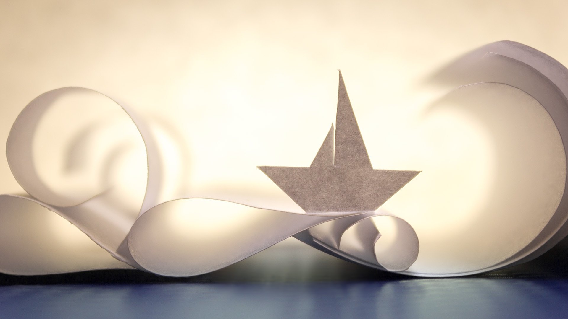 HD desktop wallpaper featuring a man-made origami paper boat crafted from white paper with artistic curled paper accents in the background.