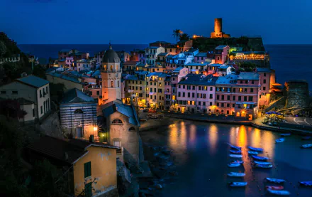 Vernazza, Italy coast at night — illuminated houses and man-made harbor with boats reflected in water, cliffside village lights; 2K Quad HD PC desktop wallpaper.
