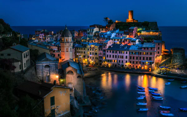 Vernazza, Italy coast at night — illuminated houses and man-made harbor with boats reflected in water, cliffside village lights; 2K Quad HD PC desktop wallpaper.