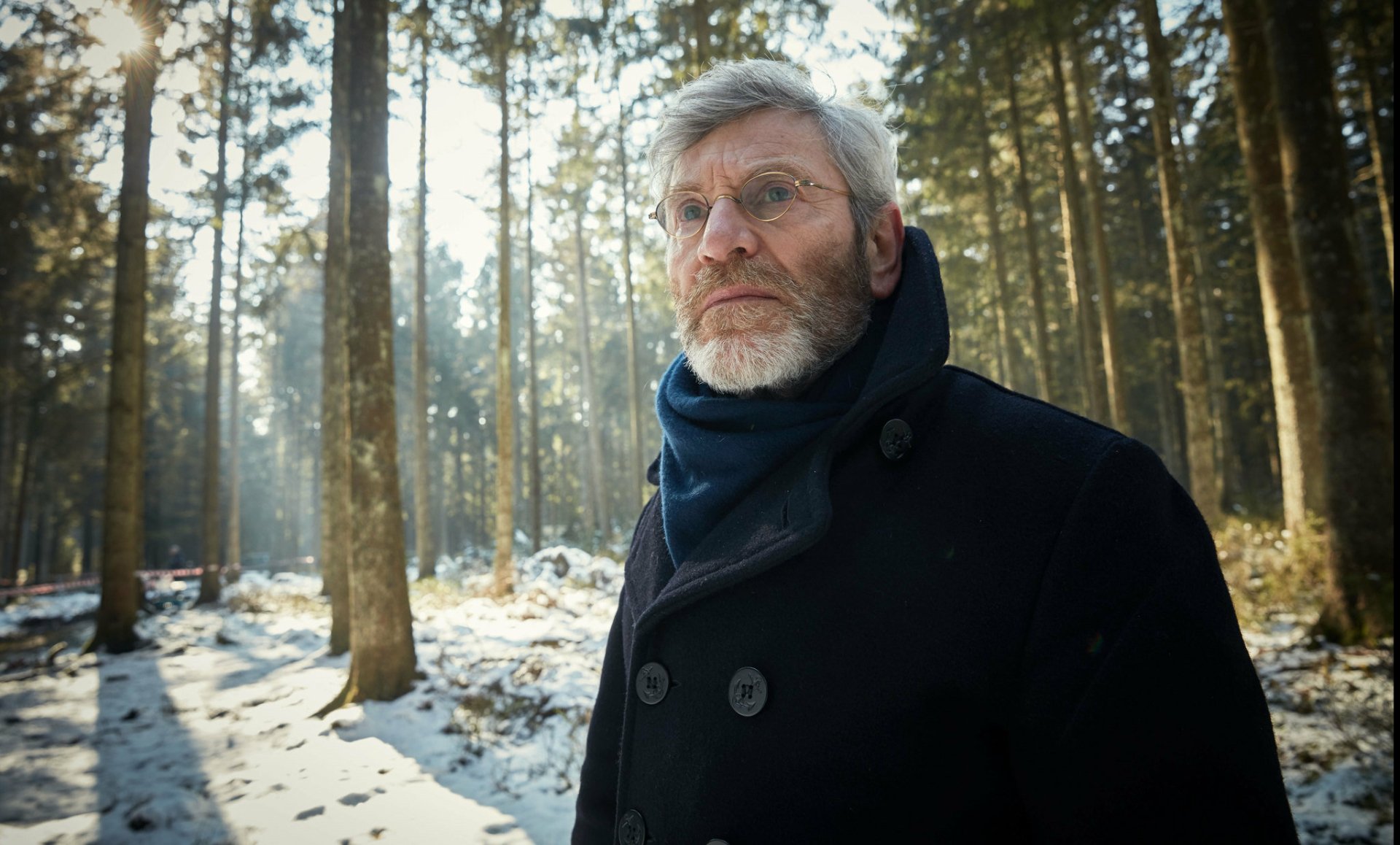 HD desktop wallpaper of a pensive man in a forest, related to The Missing, with winter trees as the background.
