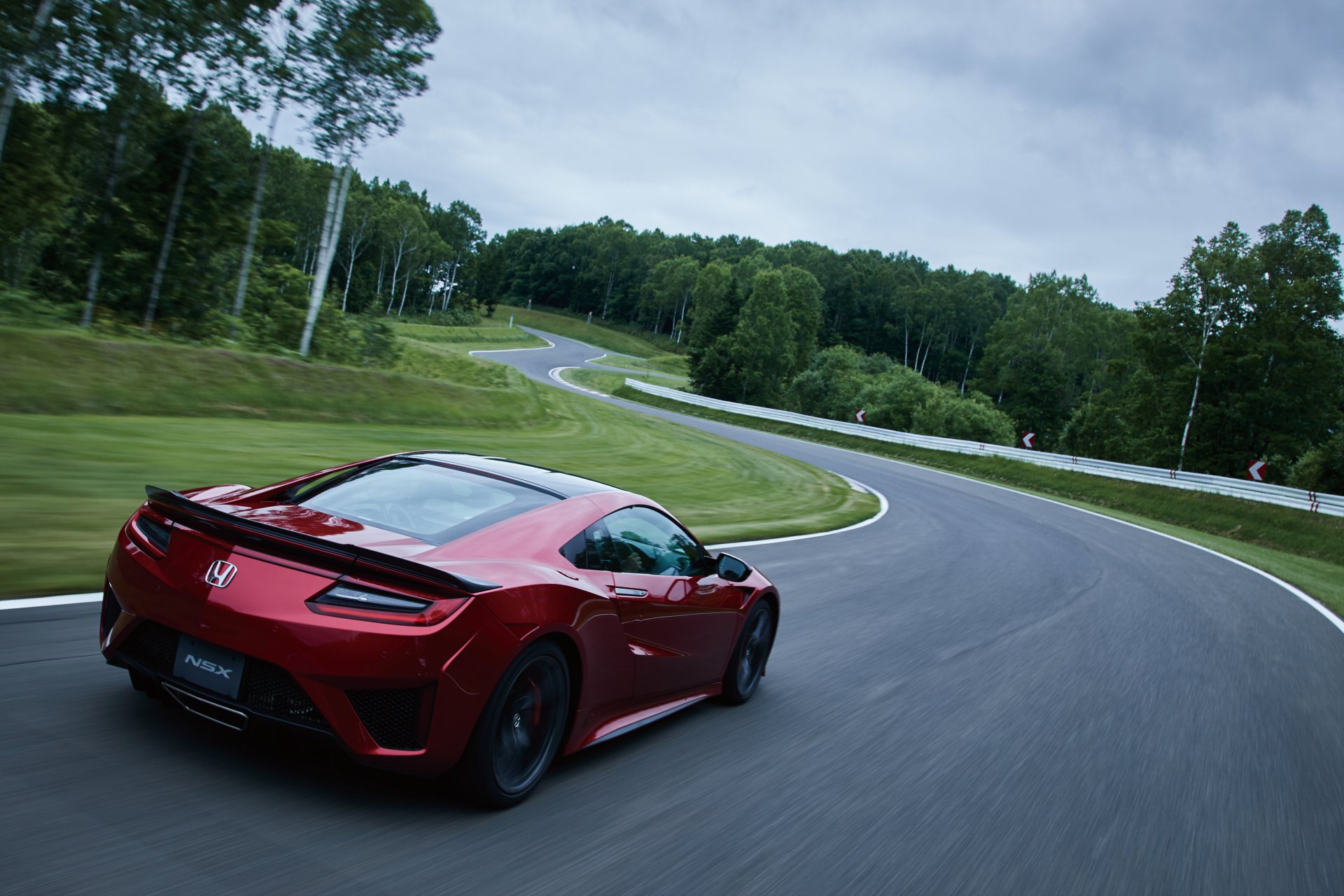 A red Honda NSX supercar speeds along a winding road surrounded by lush greenery, captured in a sharp 4K Ultra HD desktop wallpaper.