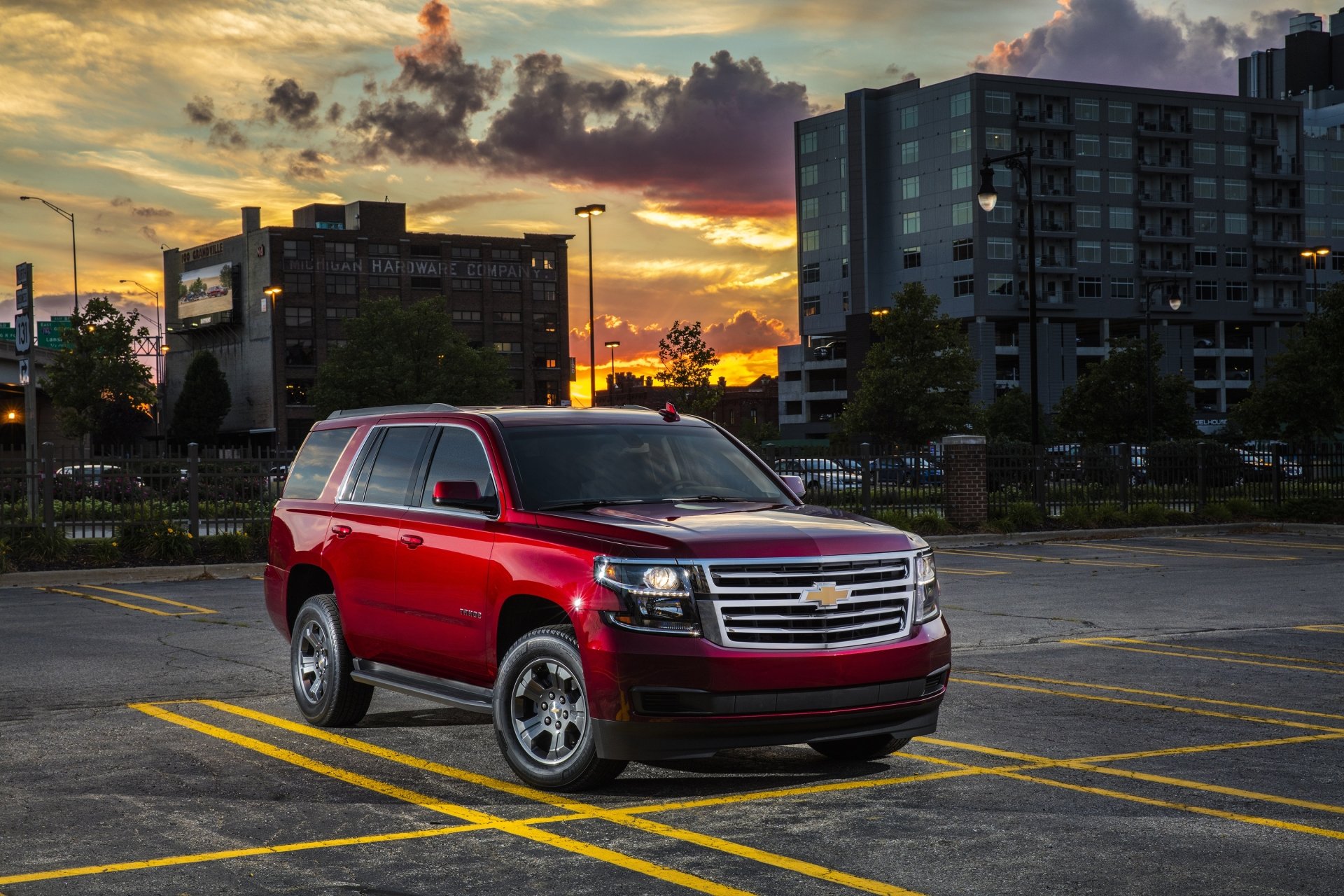 Red Chevrolet Tahoe SUV parked in an urban lot at sunset with buildings in the background, featured as an HD PC desktop wallpaper and background.