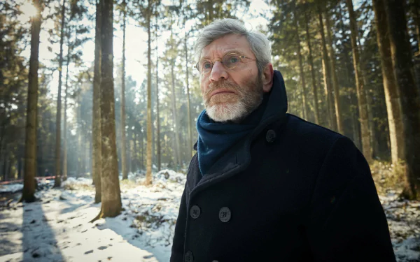HD desktop wallpaper of a pensive man in a forest, related to The Missing, with winter trees as the background.