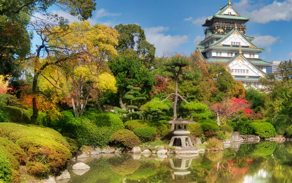Lush park surrounding Osaka Castle in Japan, featuring vibrant autumn foliage and a serene pond reflecting the historic man-made landmark.