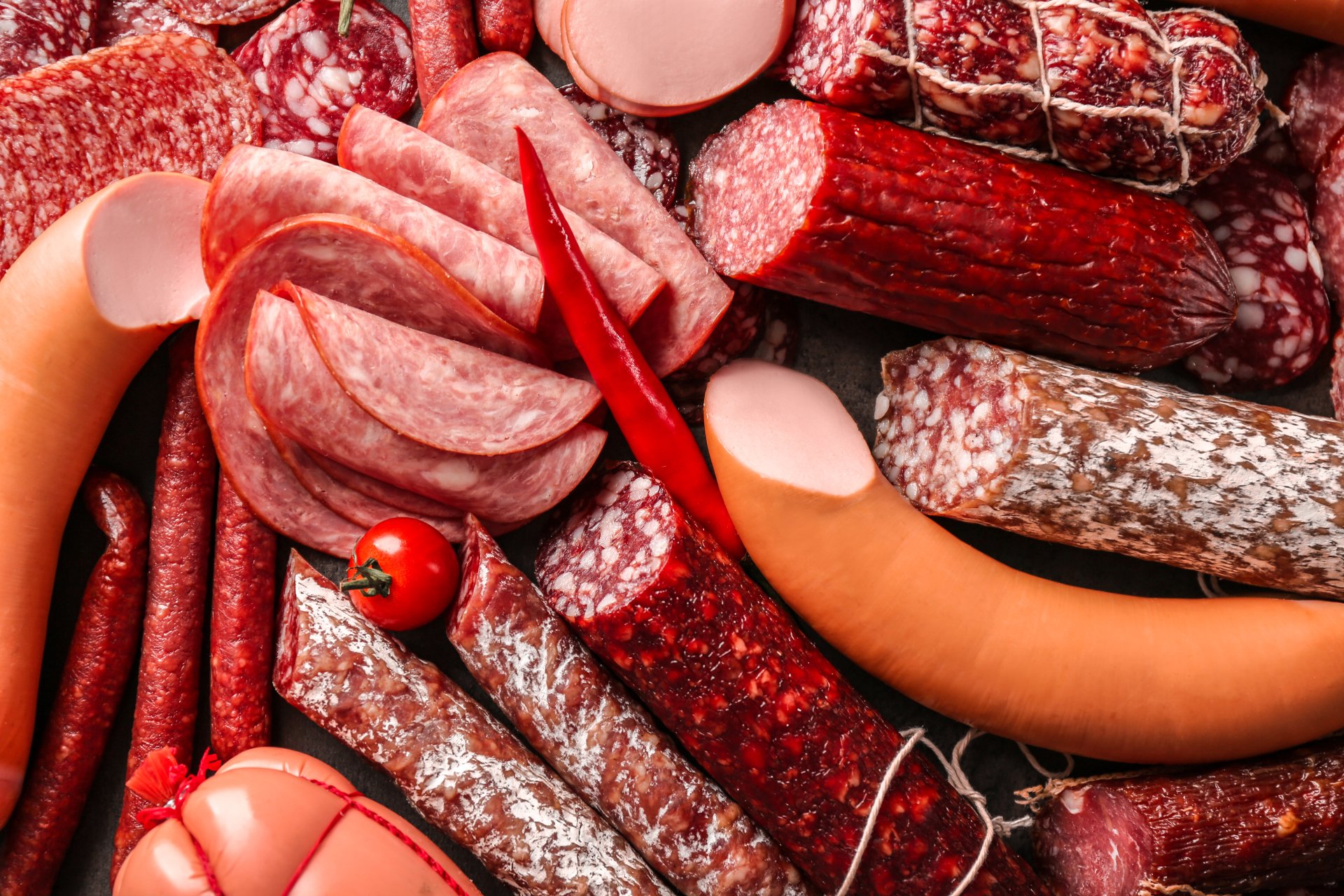 4K Ultra HD desktop wallpaper featuring a vibrant assortment of various cured and smoked meats, including sausages, salami, and sliced cuts with a chili pepper and cherry tomato accent.